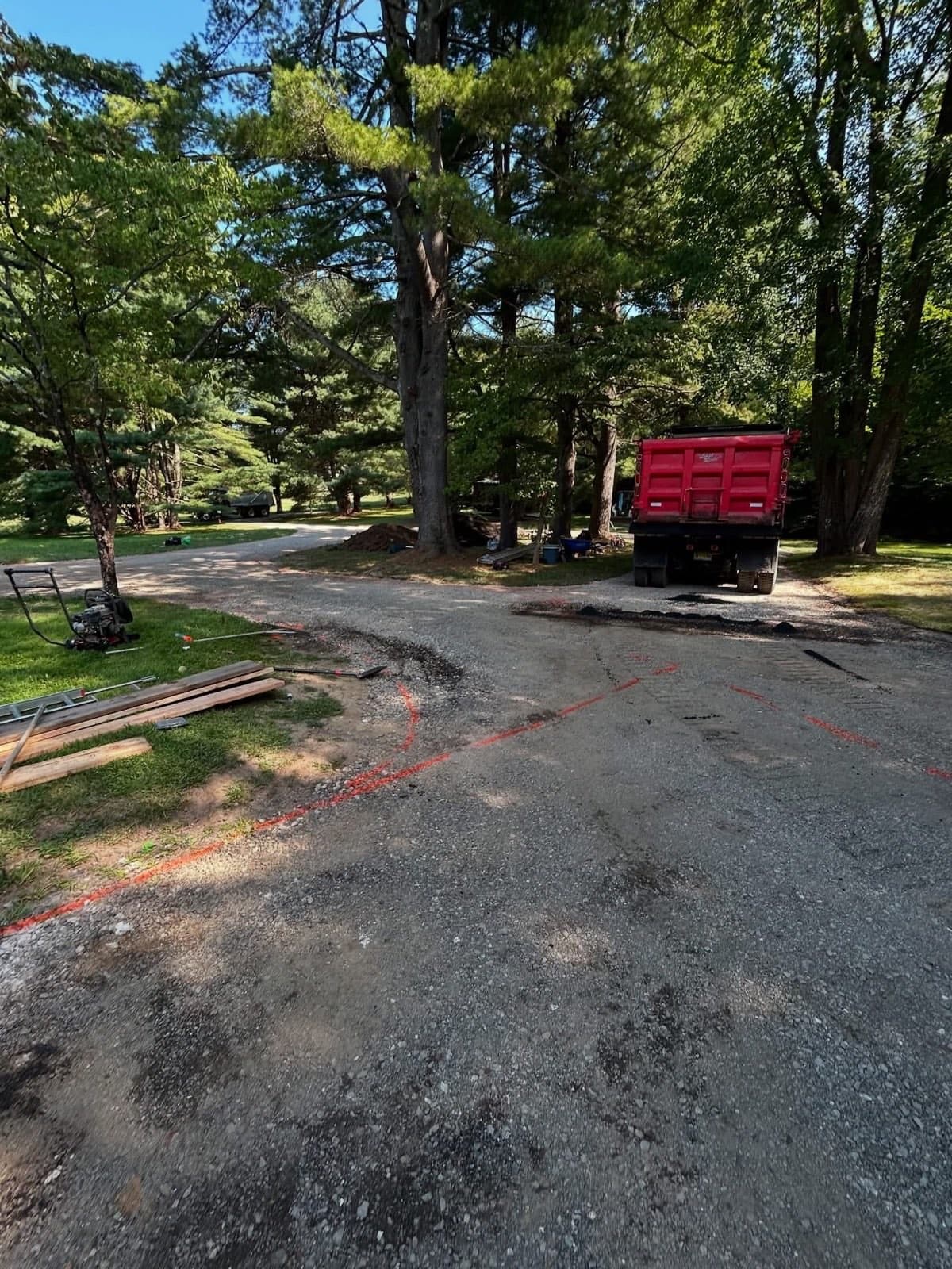 Gravel base with utility paint markings, dump truck and plate compactor staged before paving