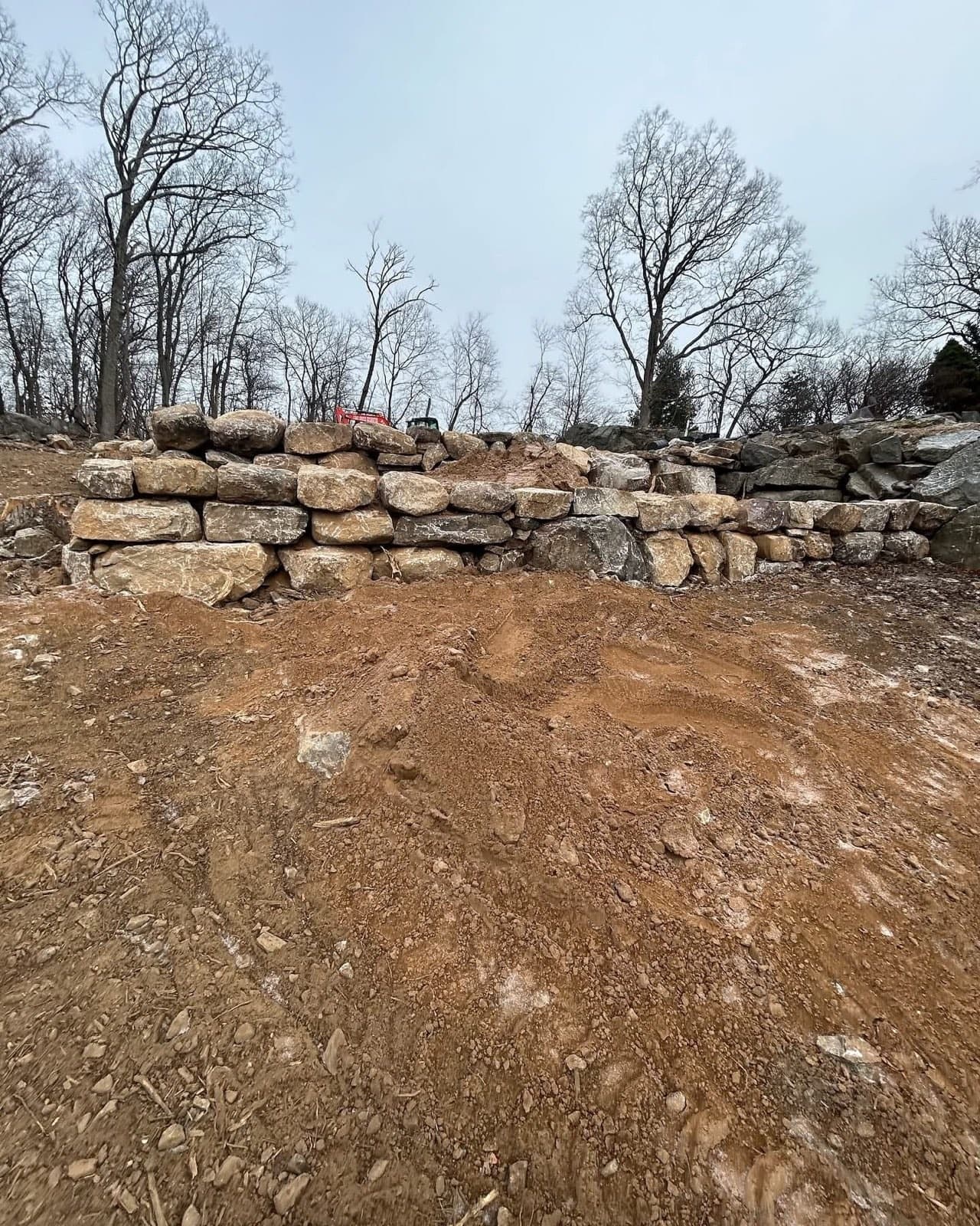 Dry stacked boulder retaining wall under construction on a cleared slope