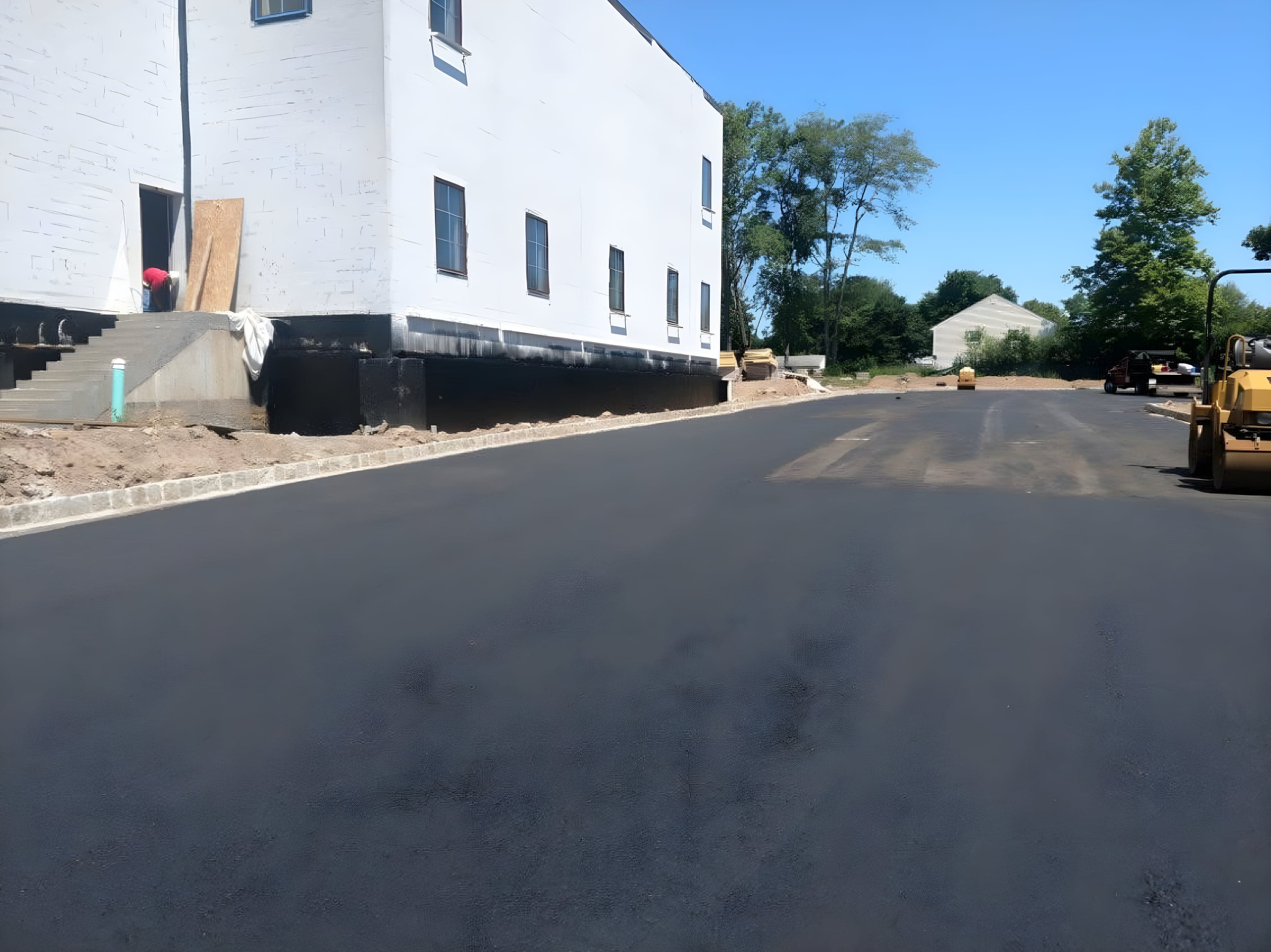 Fresh asphalt lot laid alongside a white commercial building with a roller in the background