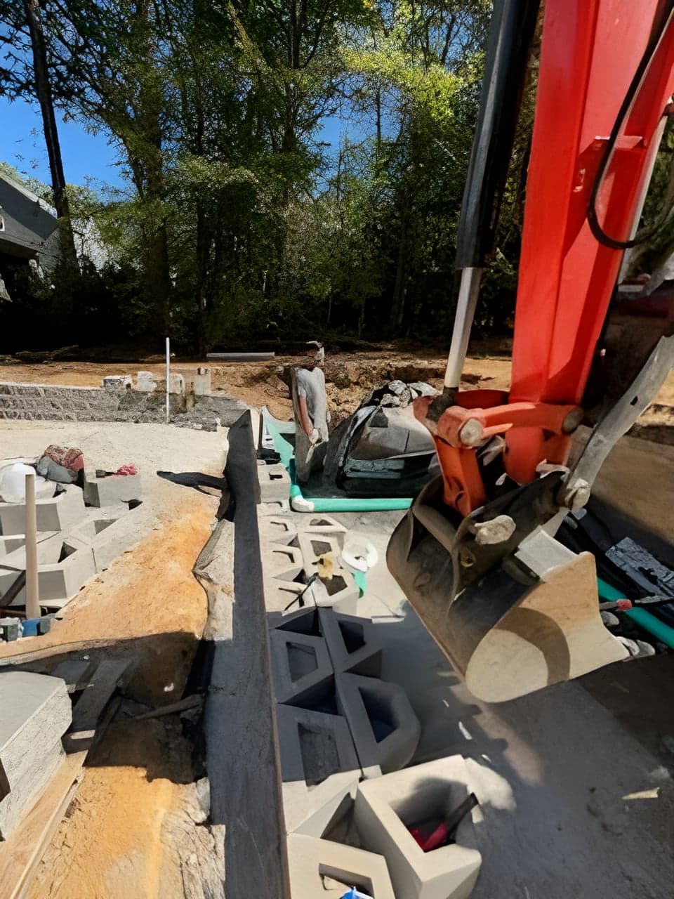 Excavator bucket placing drainage cell blocks along a green pipe run