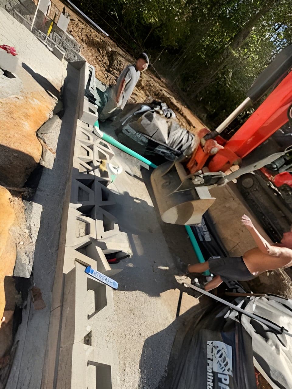 Crew setting drainage cell blocks along a gravel base with green pipe in the trench