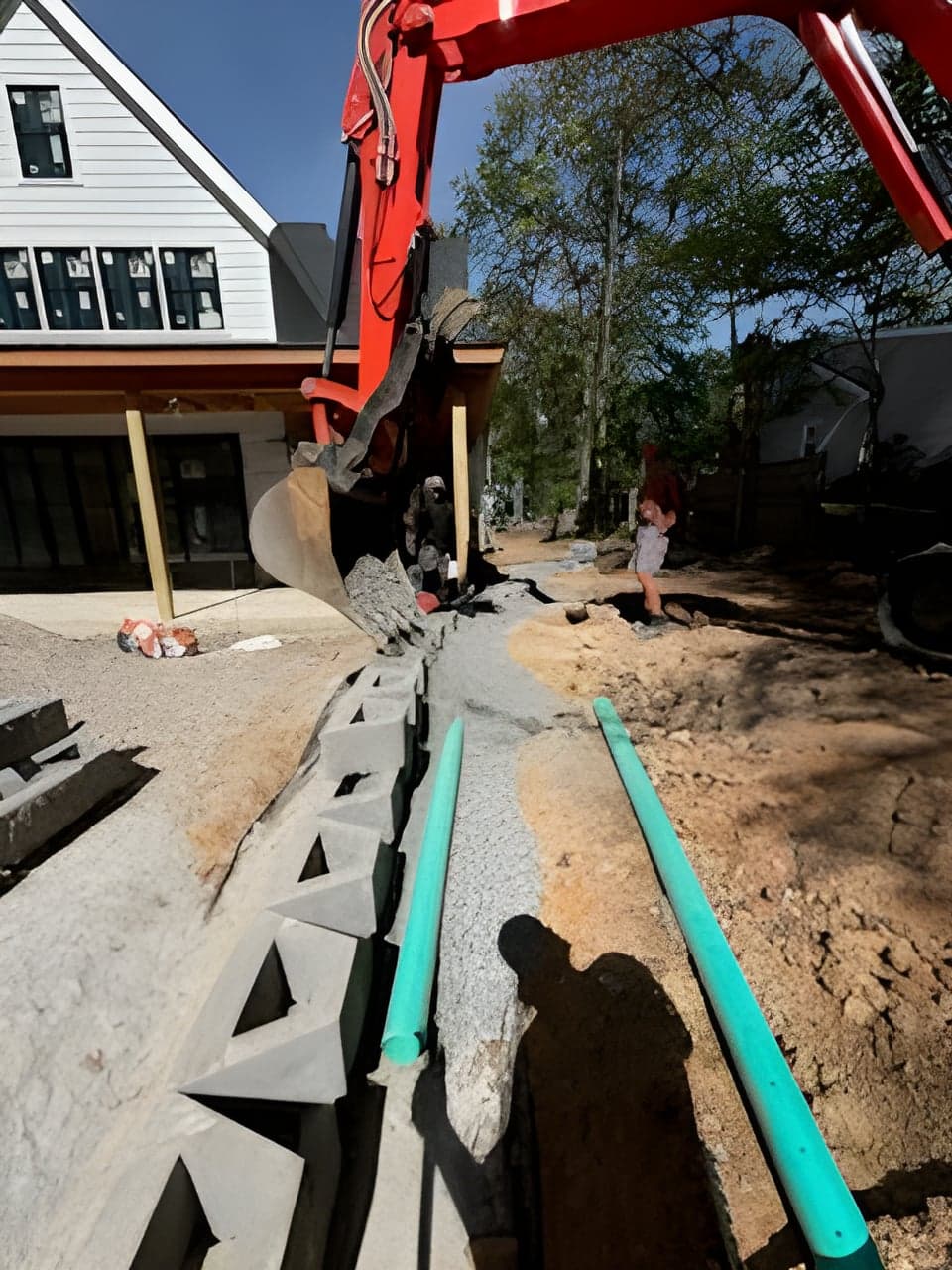 Excavator installing a drainage cell wall and green pipe beside a new build home