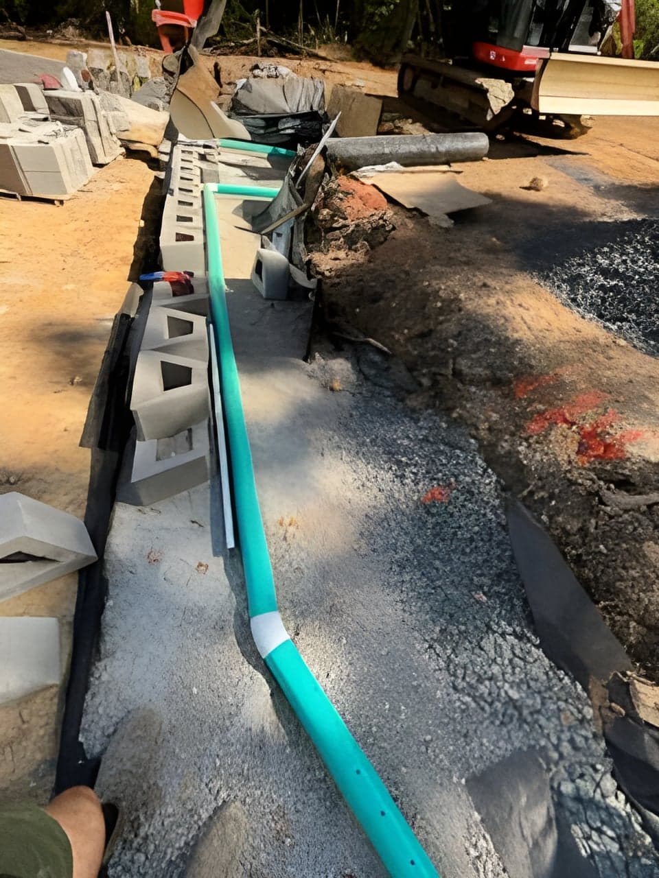 Green drainage pipe running beside a drainage cell block wall with an excavator behind
