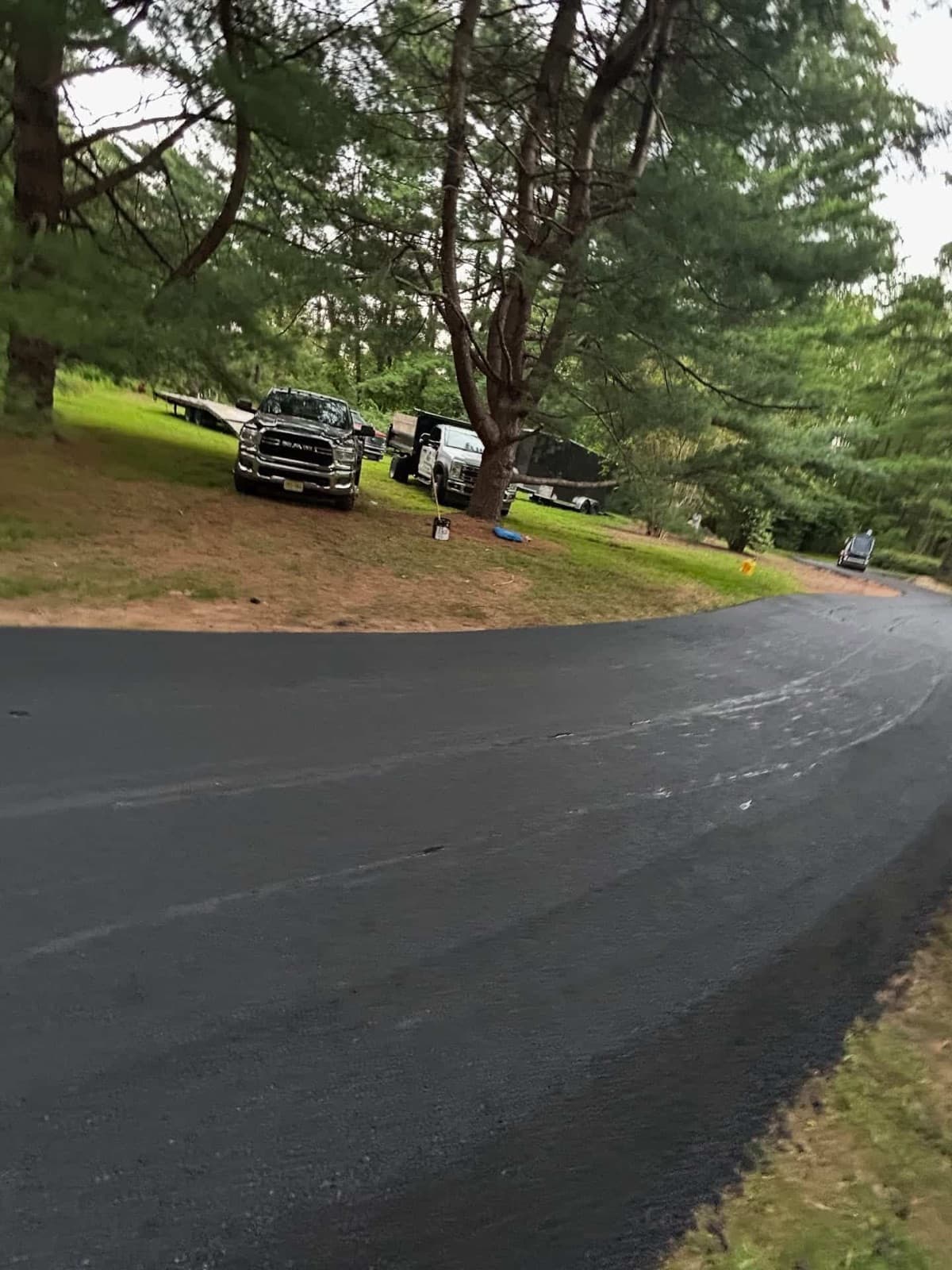 Fresh rolled asphalt curve with work trucks and an equipment trailer parked above