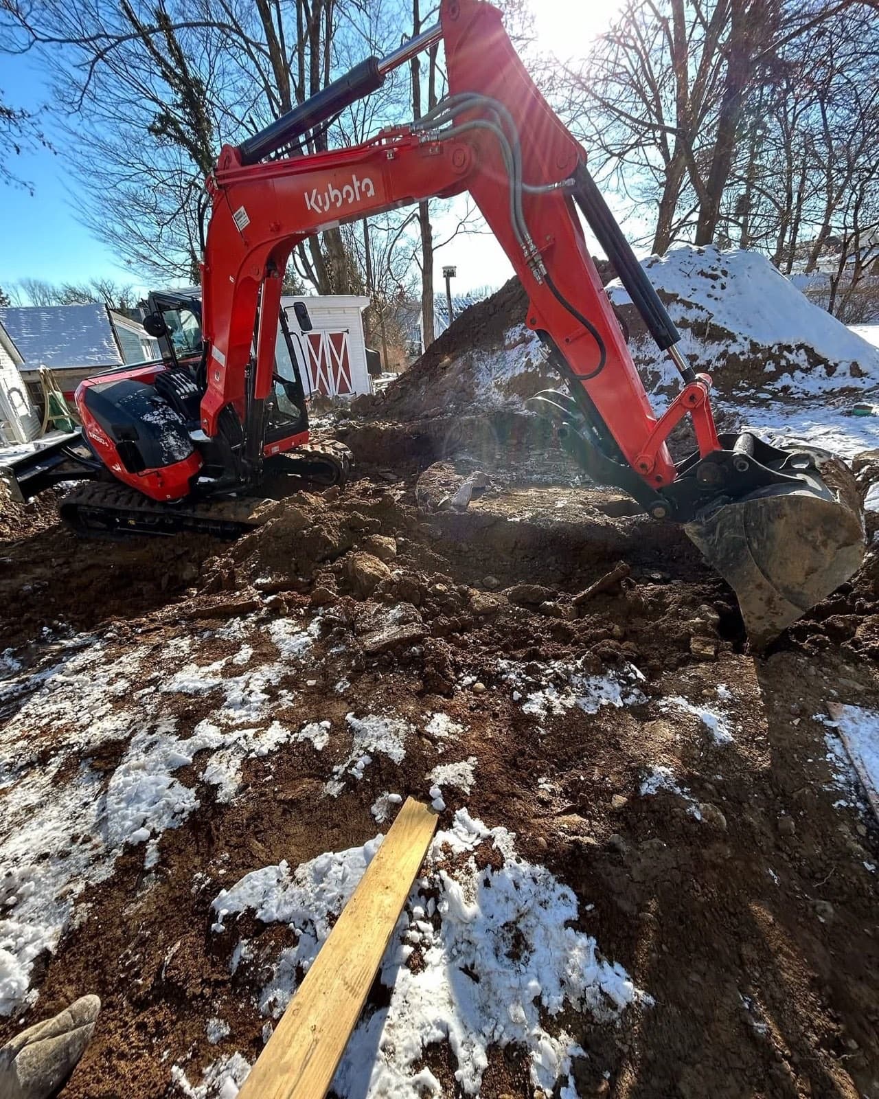 Excavator trenching a snowy foundation dig under a clear winter sky