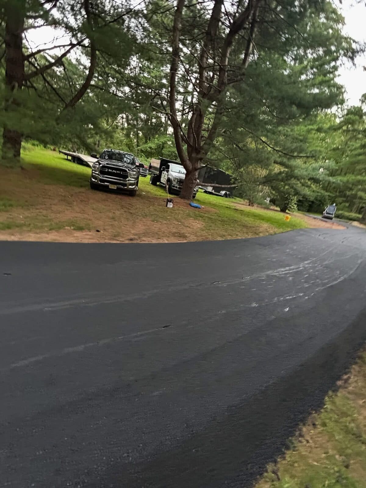Freshly paved black asphalt driveway curving past a green lawn