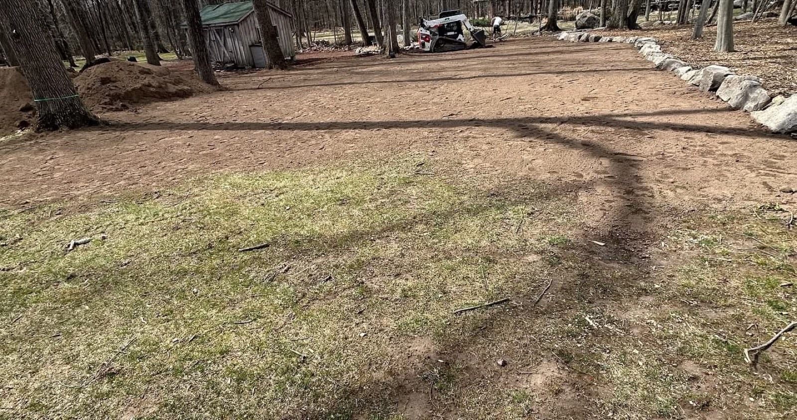 Leveled dirt pad edged with boulders and a skid steer working at the tree line