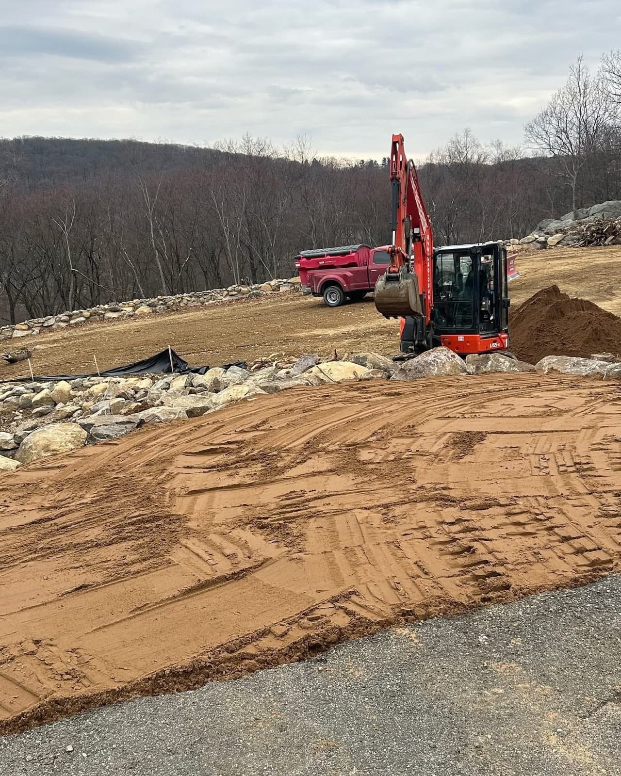 Mini excavator grading a hilltop pad edged with boulder walls