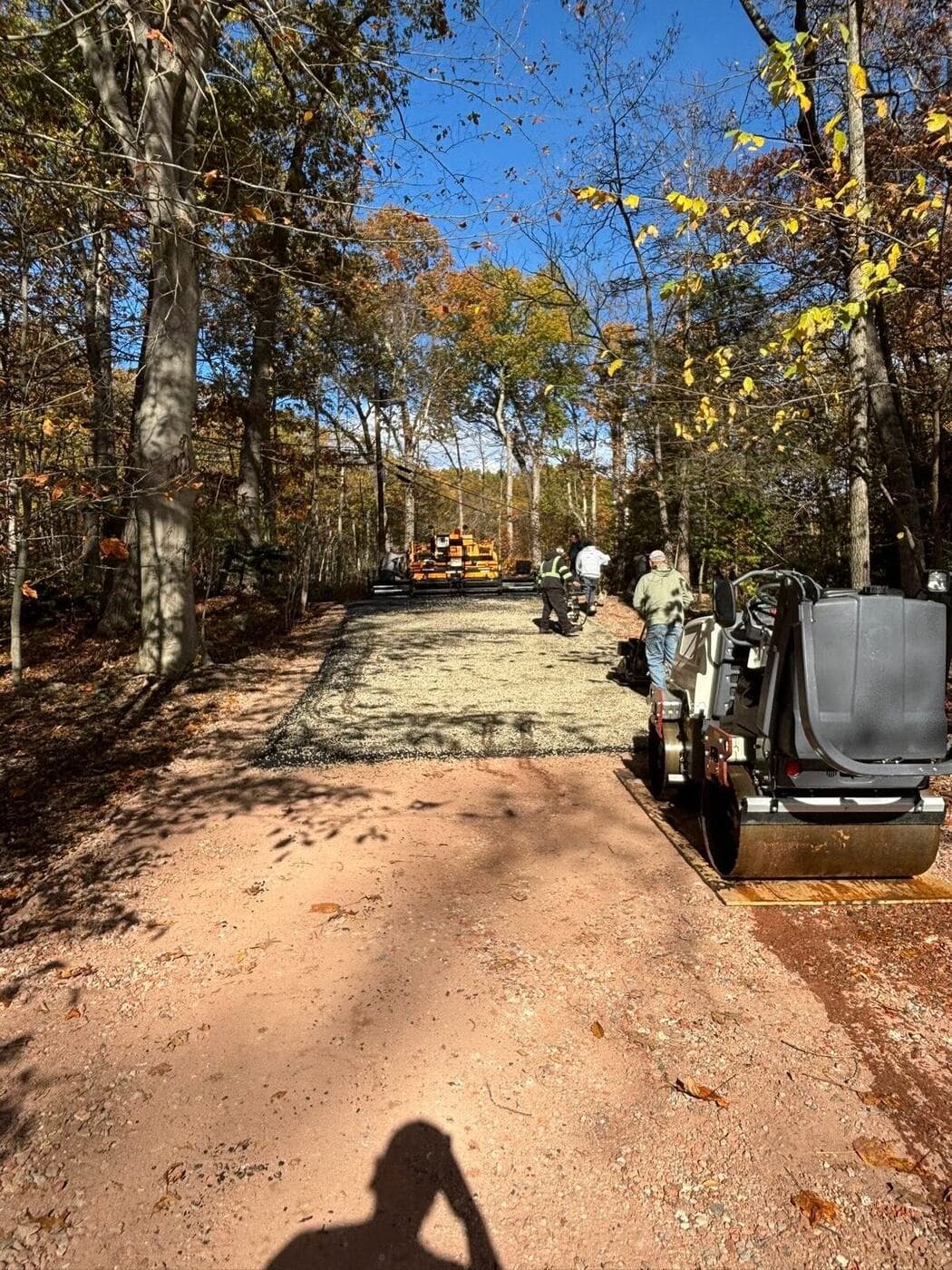 Excavated driveway with fresh gravel base being compacted before paving