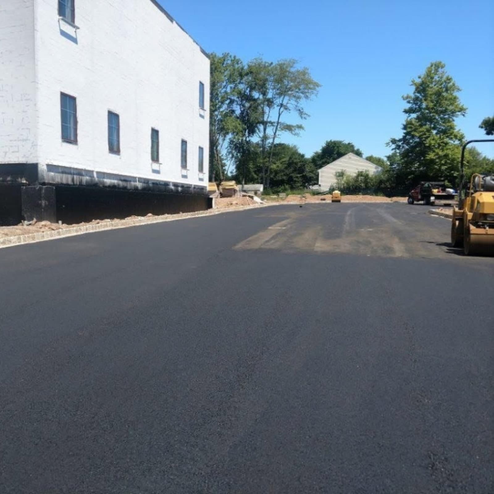 Expanse of fresh asphalt beside a commercial building with a roller working the far edge