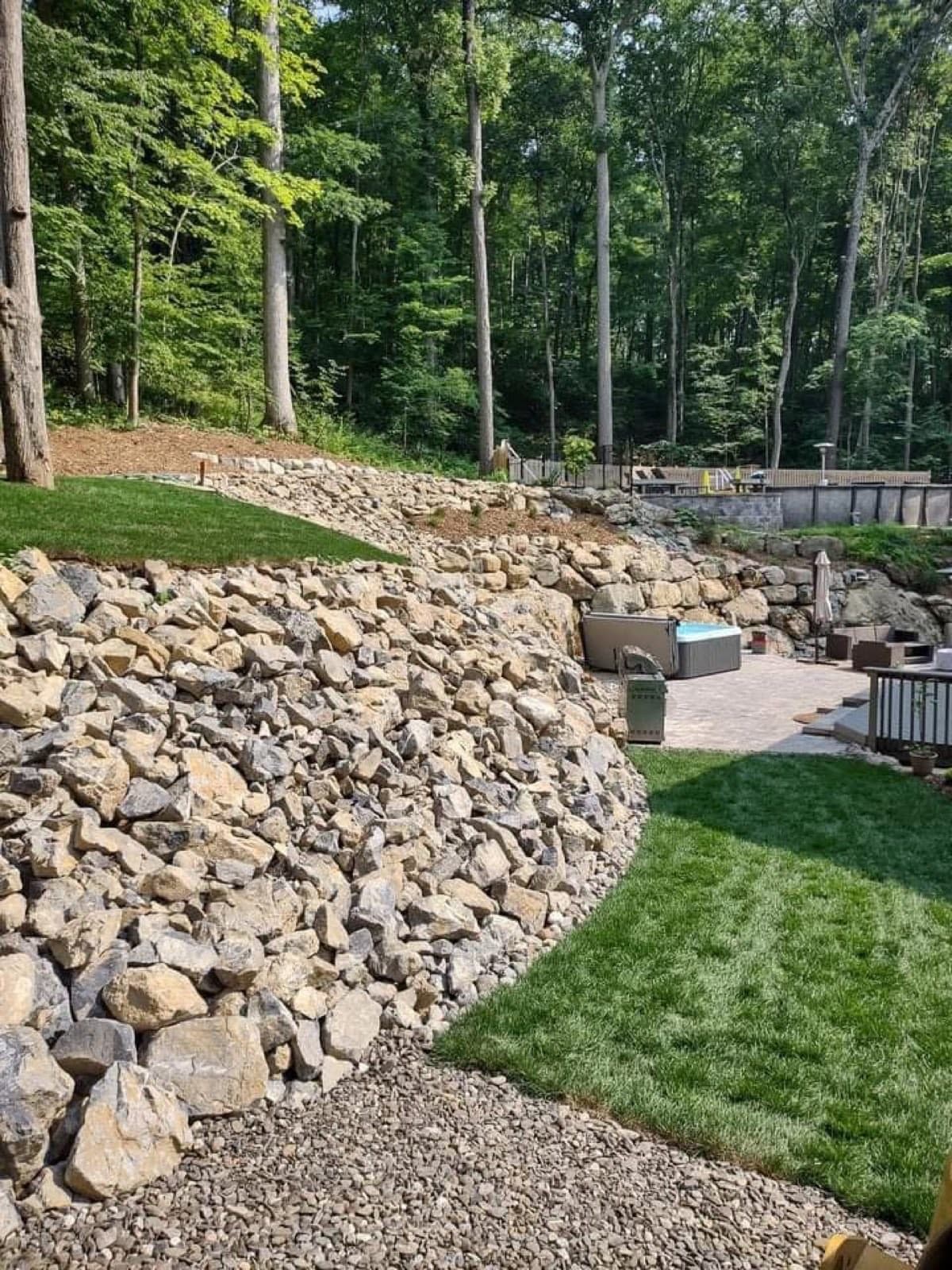 Rock riprap slope above a new sod lawn with a paver patio beyond