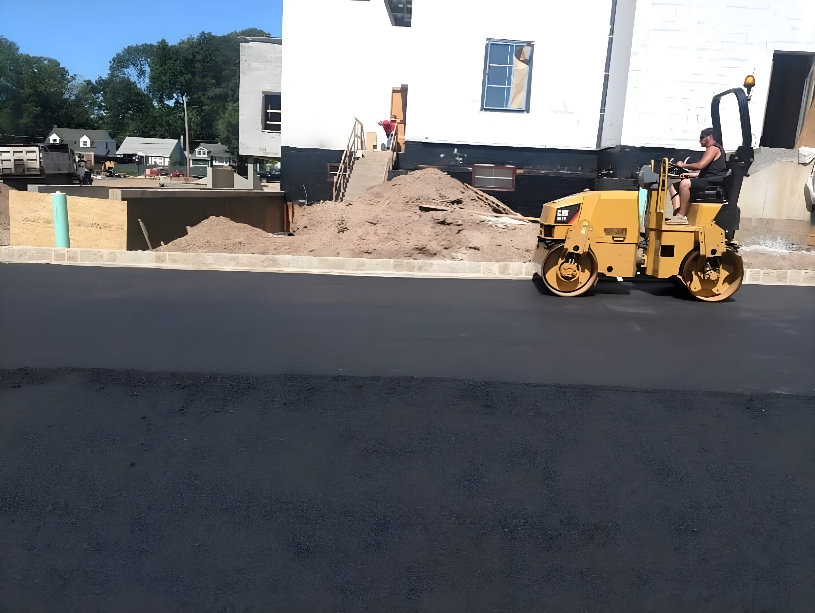 Operator on a tandem roller compacting new asphalt at a commercial building under construction