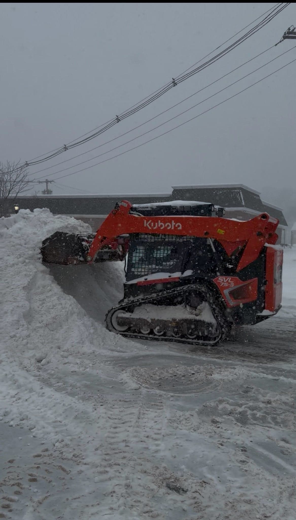 Kubota track loader pushing back a snow pile in a commercial lot during a storm