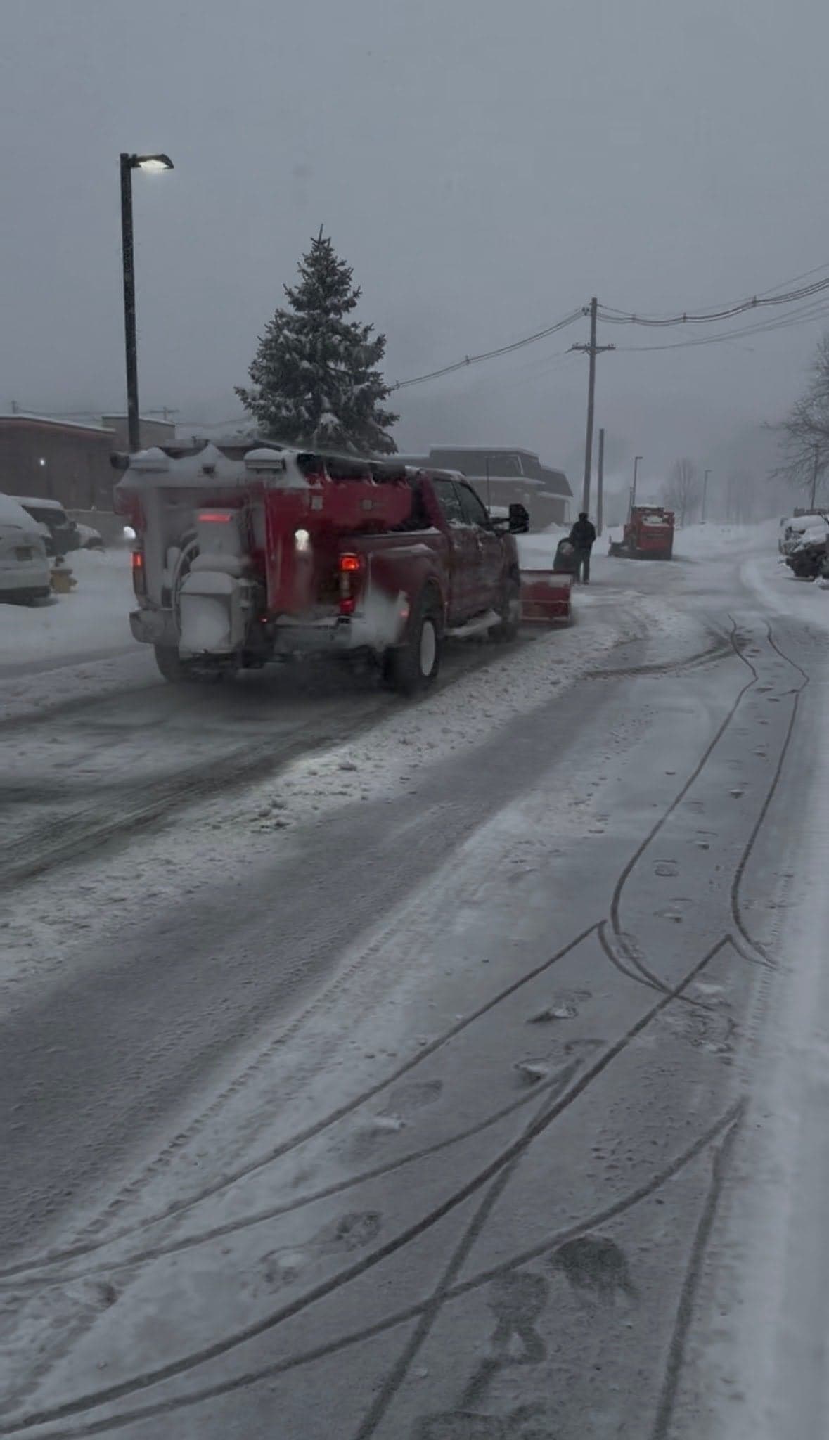 Plow truck with rear salt spreader clearing a lot while a loader works behind