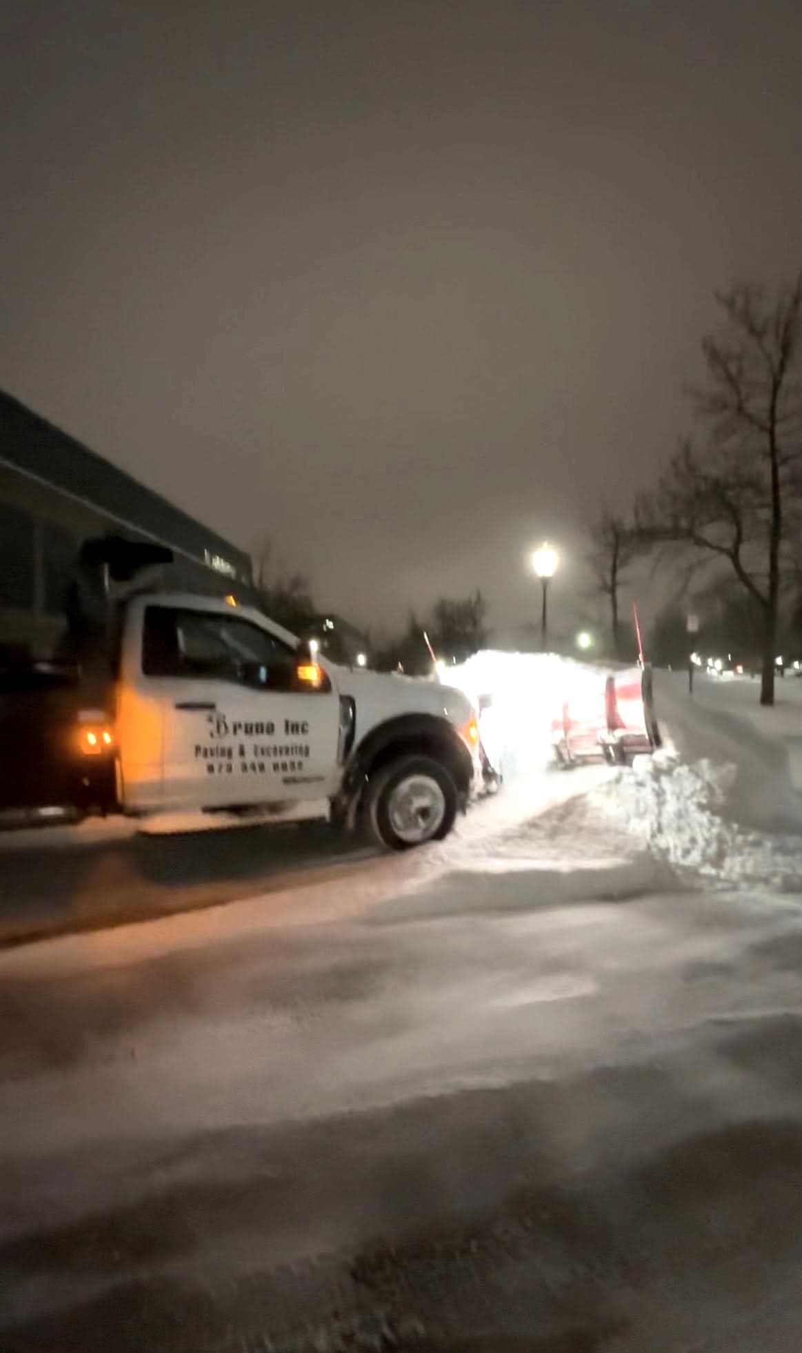 Bruno Inc plow truck clearing a commercial lot during a night snowstorm