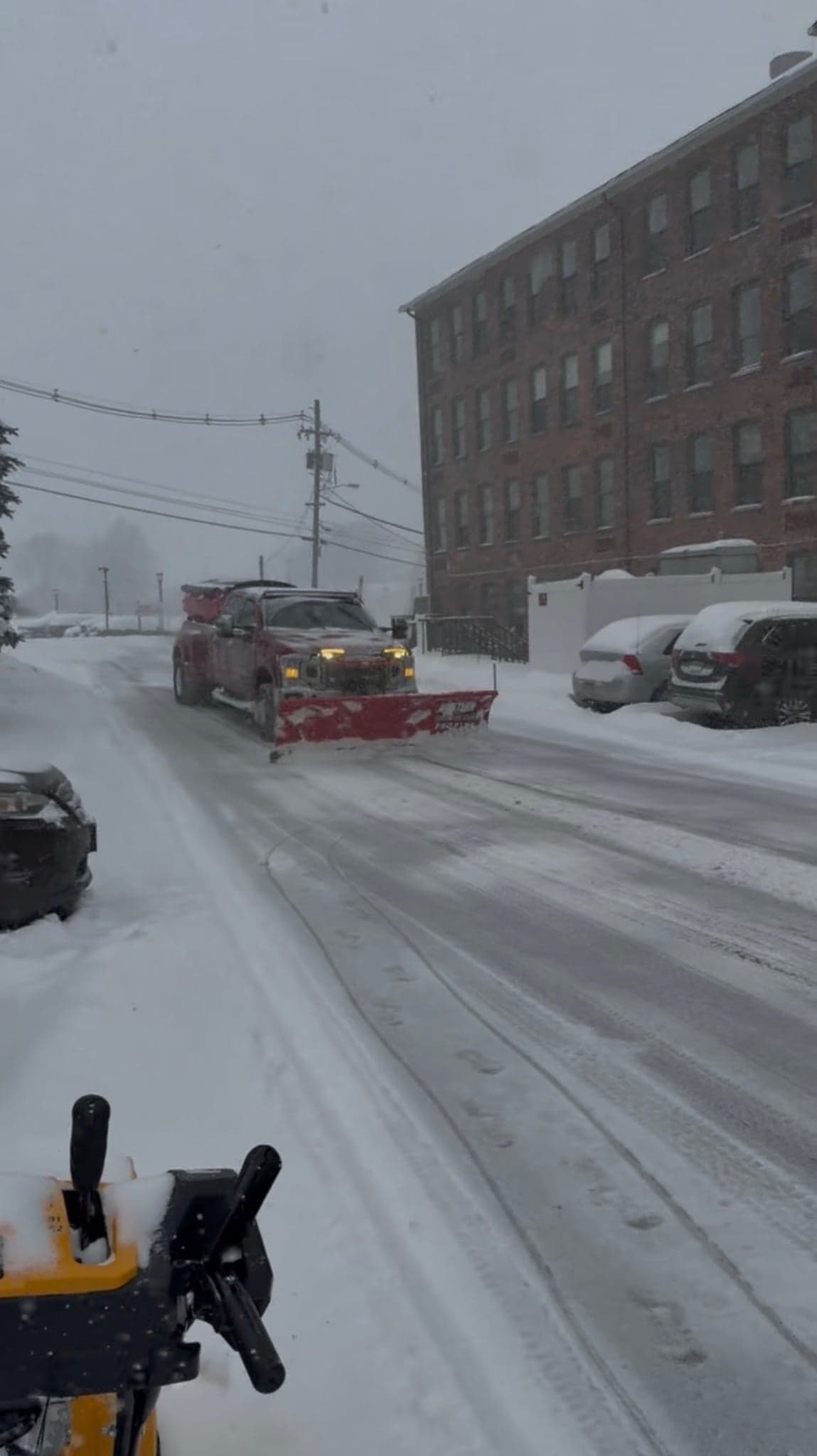 Plow truck approaching head on through a storm with a snowblower staged in the foreground