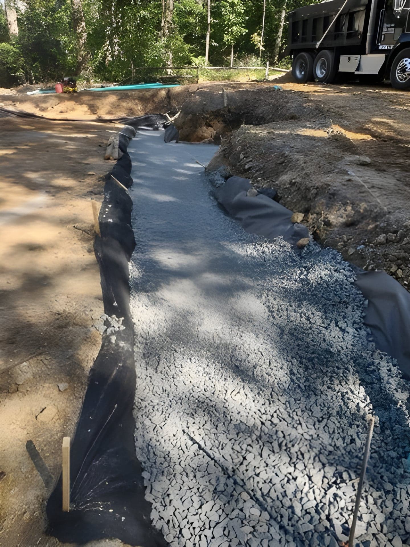Long gravel infiltration bed wrapped in filter fabric with a dump truck delivering stone