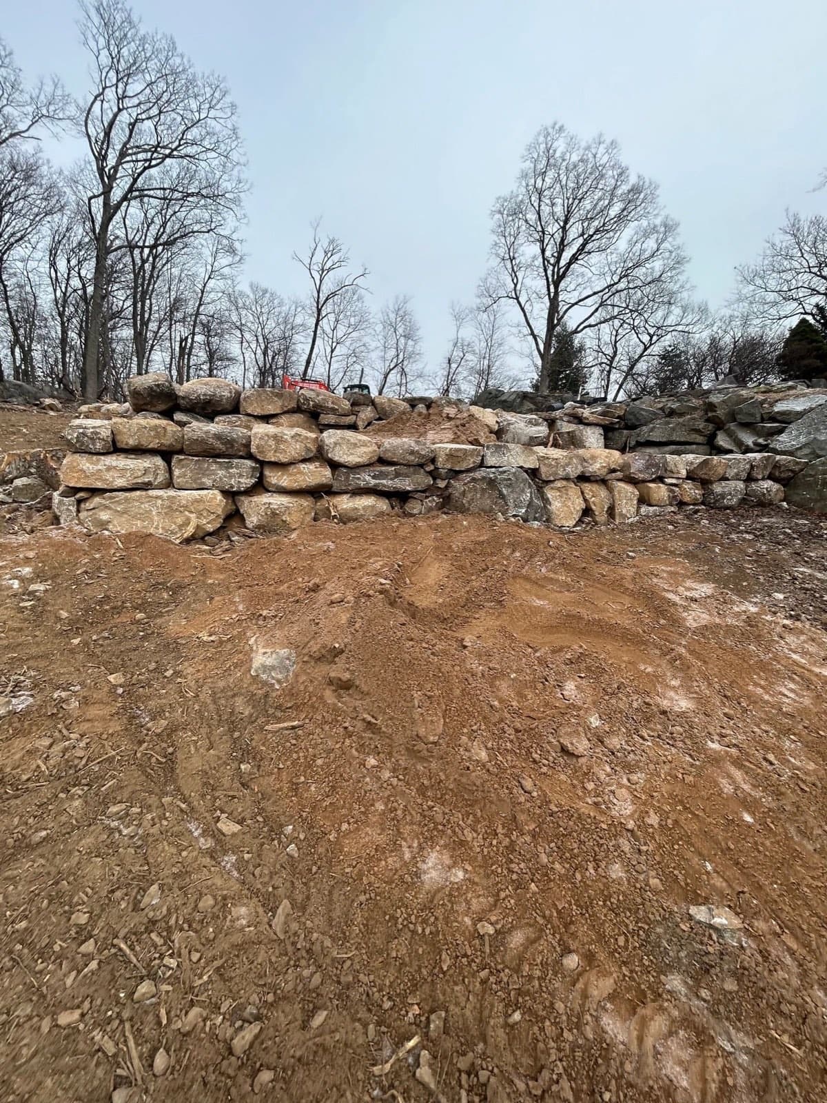 Two tiers of dry stacked boulder retaining wall viewed from the regraded slope below