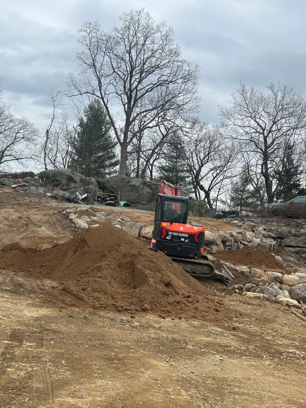 Excavator spreading topsoil against boulder retaining walls on a winter site